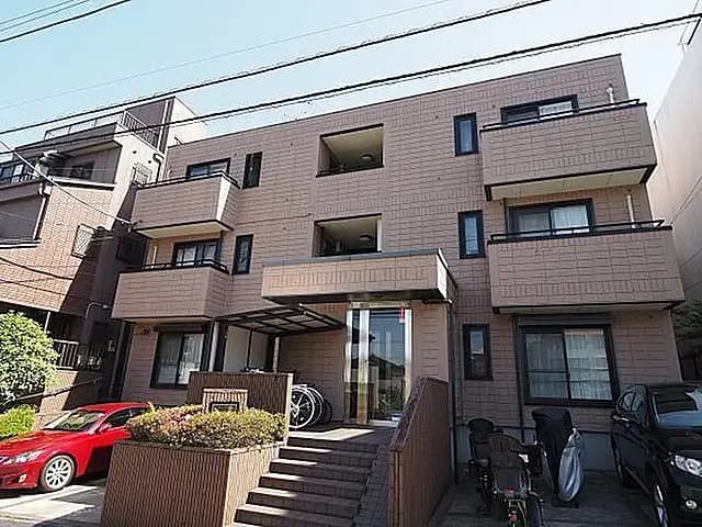 - 現代的な外観のアパートメントビル、階段とエントランス、バルコニーがある住宅の外観、周囲には駐車スペースと緑が配置されている