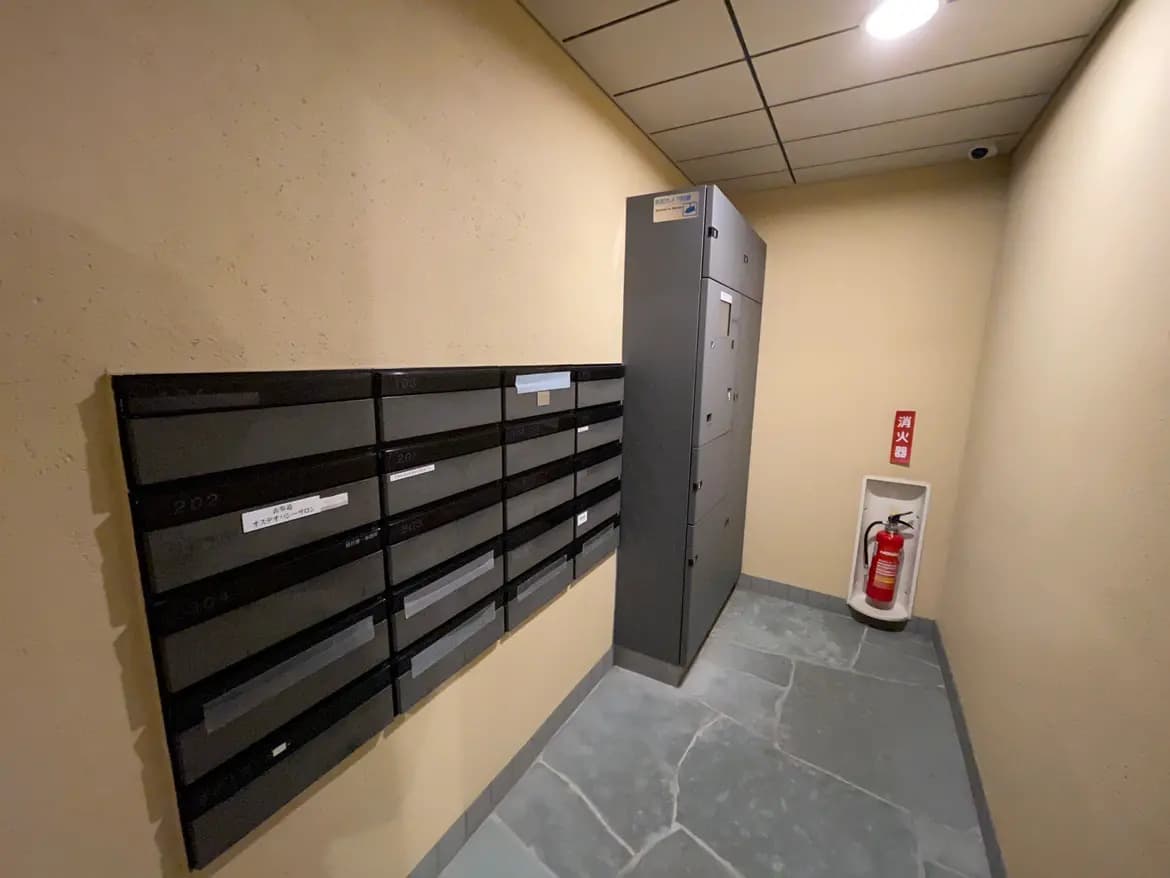 建物のエントランスにあるモダンな郵便ポストと宅配ボックス、消化器具と灰色のタイルが敷かれたフロア