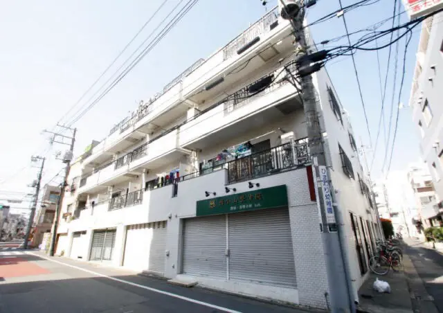 - 地元の商業施設がある住宅街の角に位置する白い外観の4階建てアパートメント、学校や公共交通機関に近い便利な立地