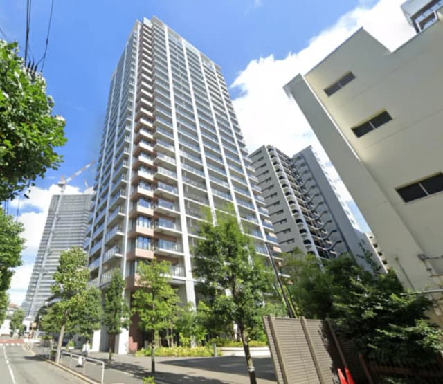 - 高層マンションの外観、青空と緑の木々に囲まれた都市の風景、周囲の建物と一緒に映る現代的なデザイン