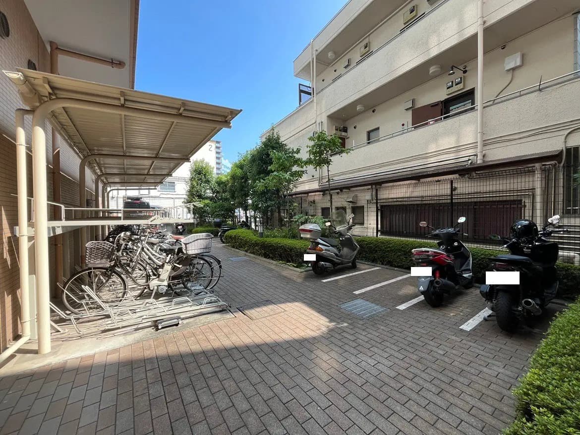 - 自転車置き場とバイク駐輪スペース、周囲には緑の植栽が施された明るい駐車場の風景