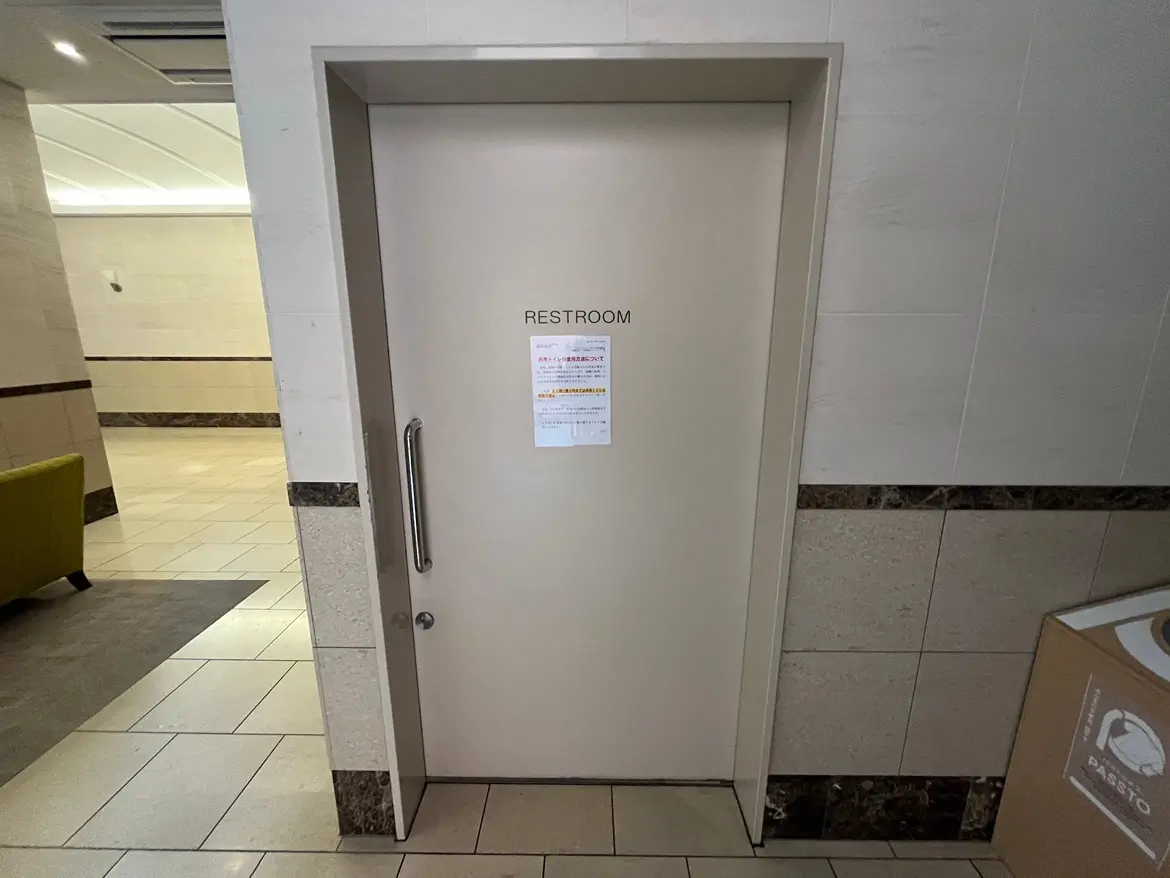 - 清潔感のあるトイレの入口、シンプルなデザインと注意書きが貼られたドア