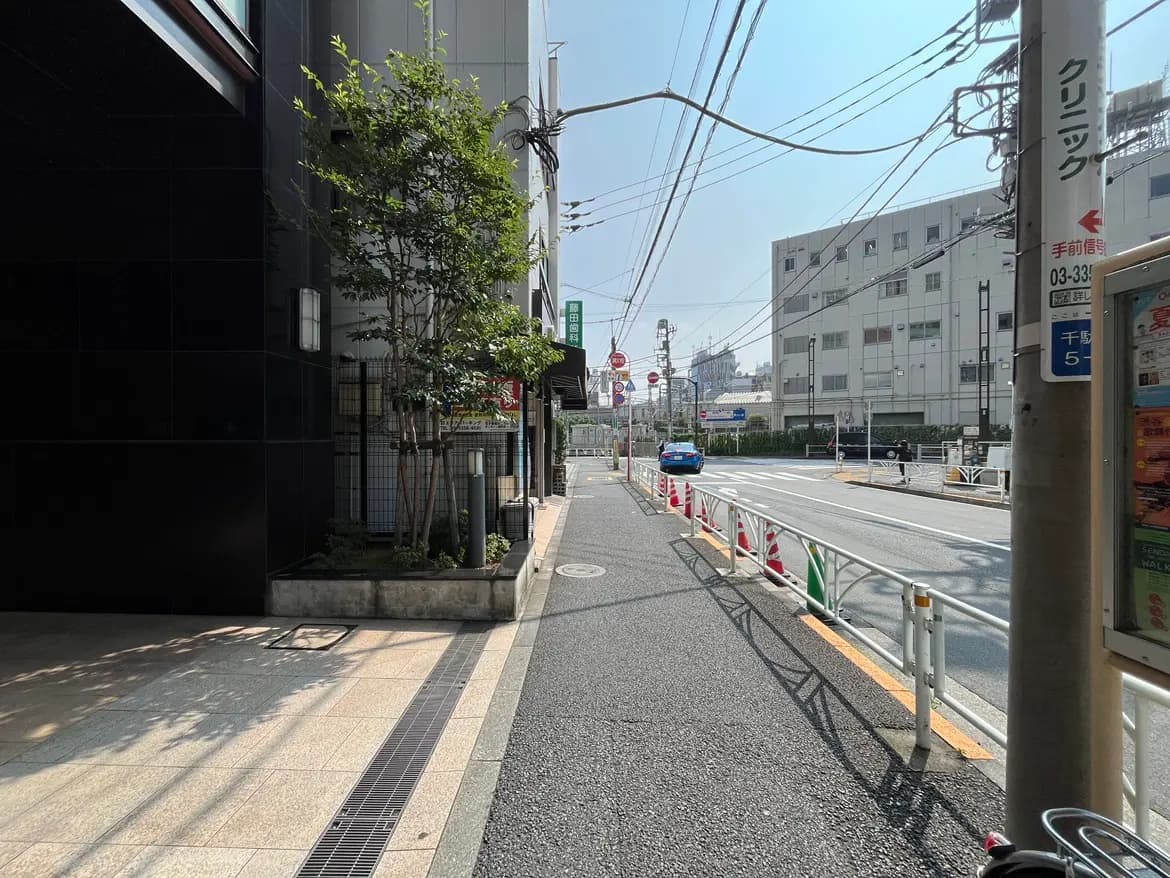 - 黒い外壁のビルと整備された歩道、近くの道路に車が走る様子、青空が広がる静かな街並み