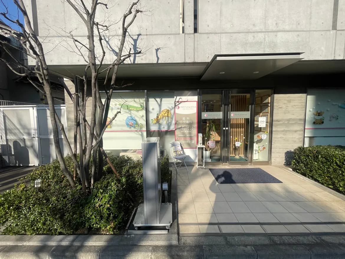 日当たりの良い通りに面したモダンな歯科医院の入り口、ガラスドアと落ち着いた色合いの外観