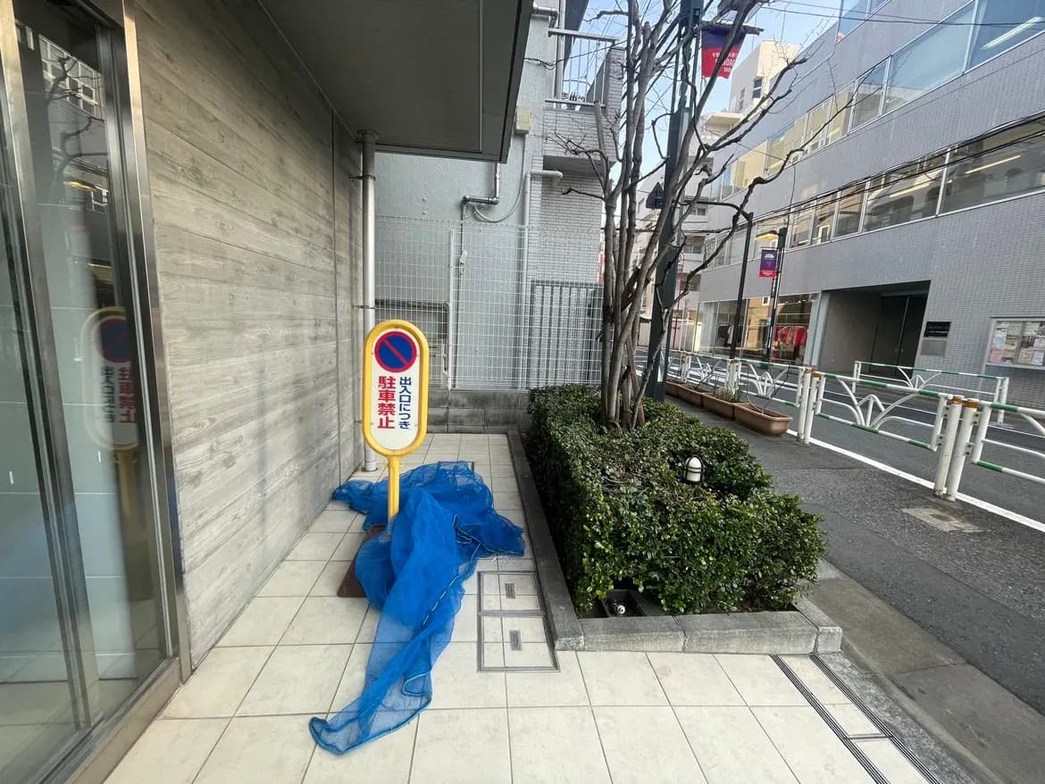 街角の歩道と駐輪場、禁止標識と青いビニールシートが置かれた景色