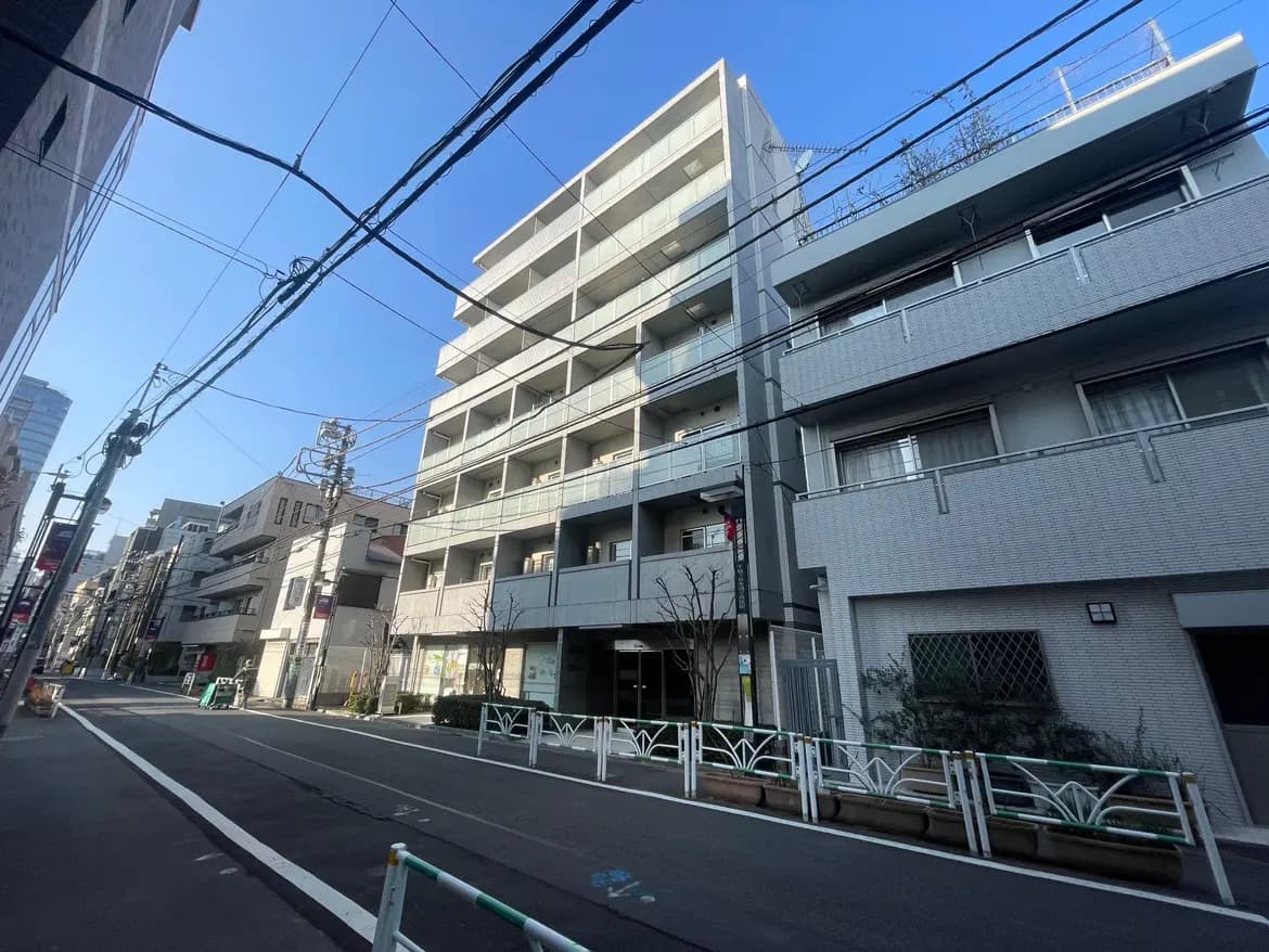 明るい日差しの中、都市の住宅街に位置する現代的なマンションと商業施設が並ぶ風景