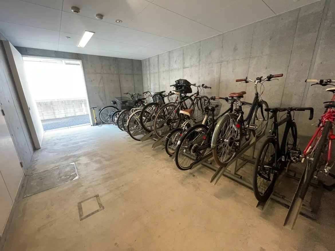 コンクリートの壁が特徴的な自転車駐車場、整然と並んだ多様な自転車、明るい自然光が差し込む空間