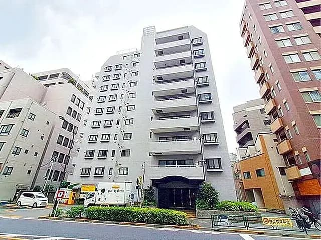 - 都市部に位置するモダンな外観のマンション、周囲には高層ビルと緑豊かな植栽がある景観