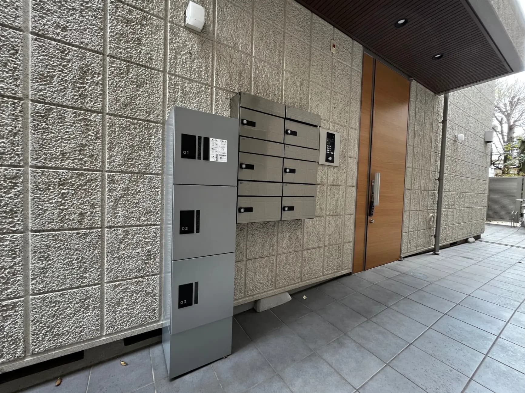 モダンなマンションのエントランスに設置された宅配ボックスと木目調の玄関扉