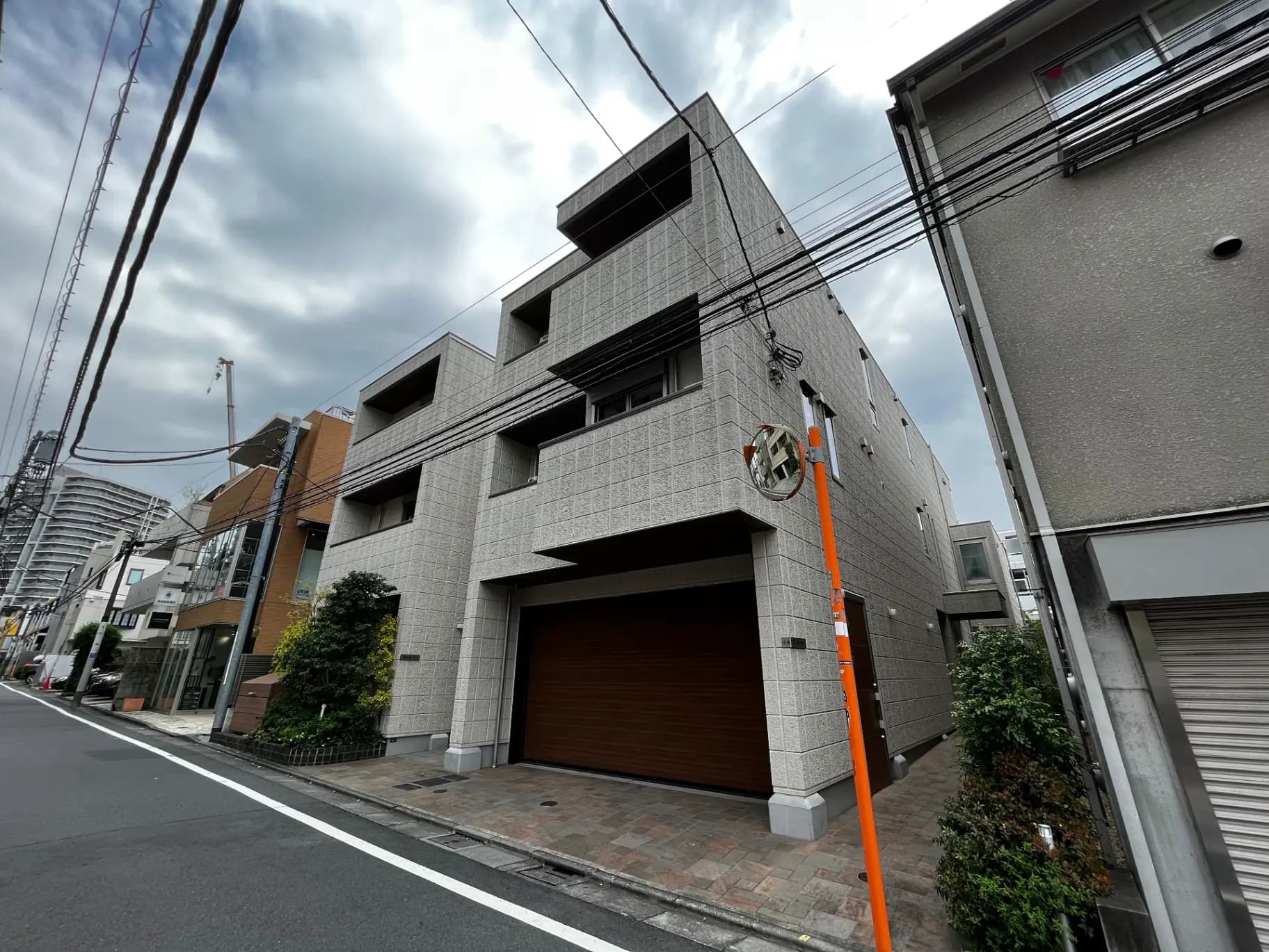 都市部に立つモダンなグレーの外観の建物、ガレージ付きの住宅、街路樹と曇り空