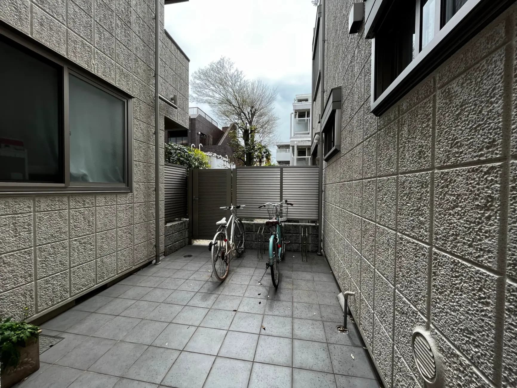 都市型住宅の外観、石造りの壁と広々としたスペース、自転車が置かれた閑静なエリア