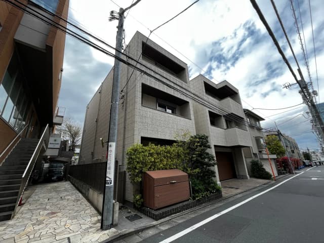 現代的なデザインのマンション外観、石畳の歩道、都市の電線と青空