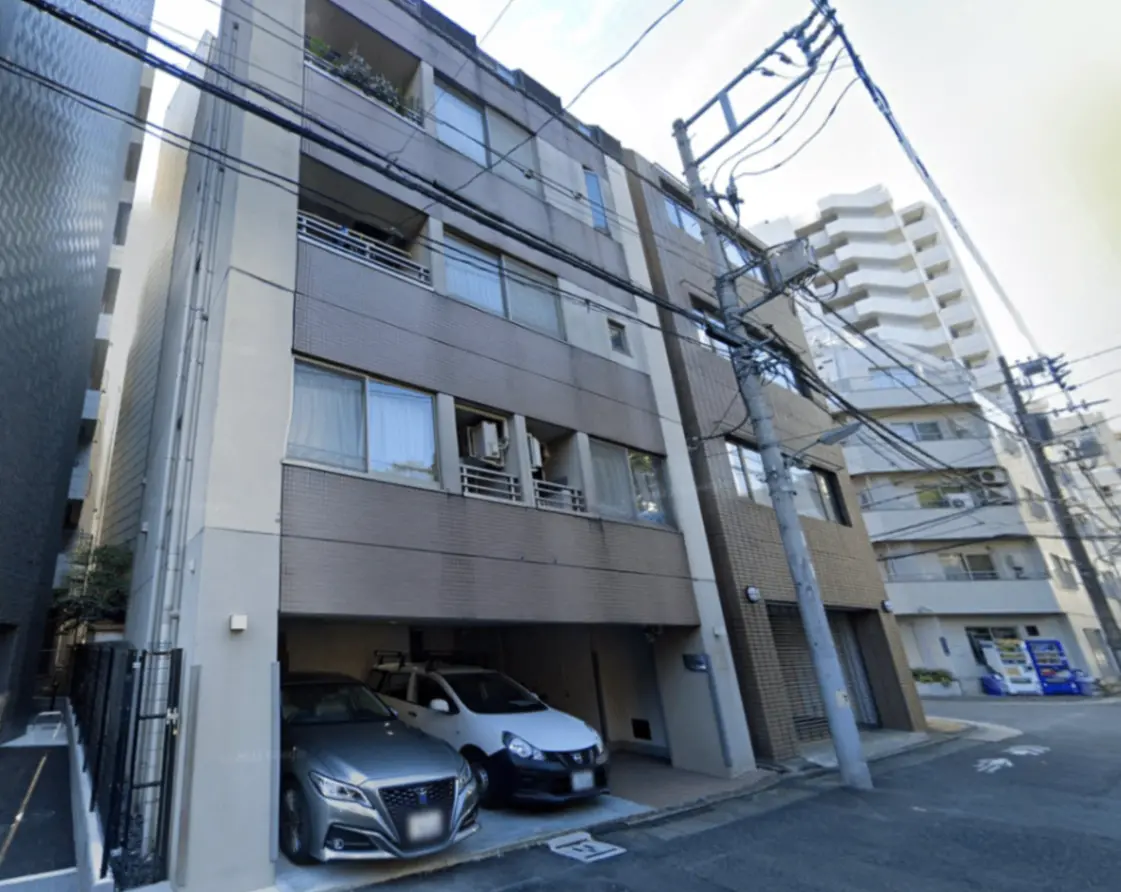 - モダンな外観のアパートメントビル、駐車スペースに並ぶ2台の車と周囲の電柱が見える都市の風景