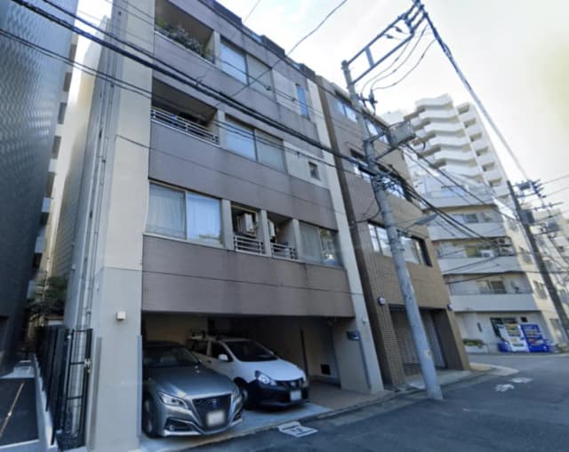 - モダンな外観のアパートメントビル、駐車スペースに並ぶ2台の車と周囲の電柱が見える都市の風景