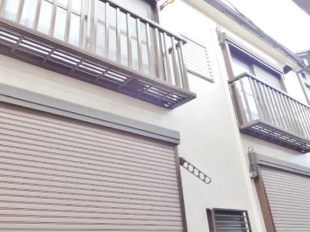 - 二階建ての住宅の外観、バルコニーとシャッター付きの窓があり、白い壁が特徴的なデザイン