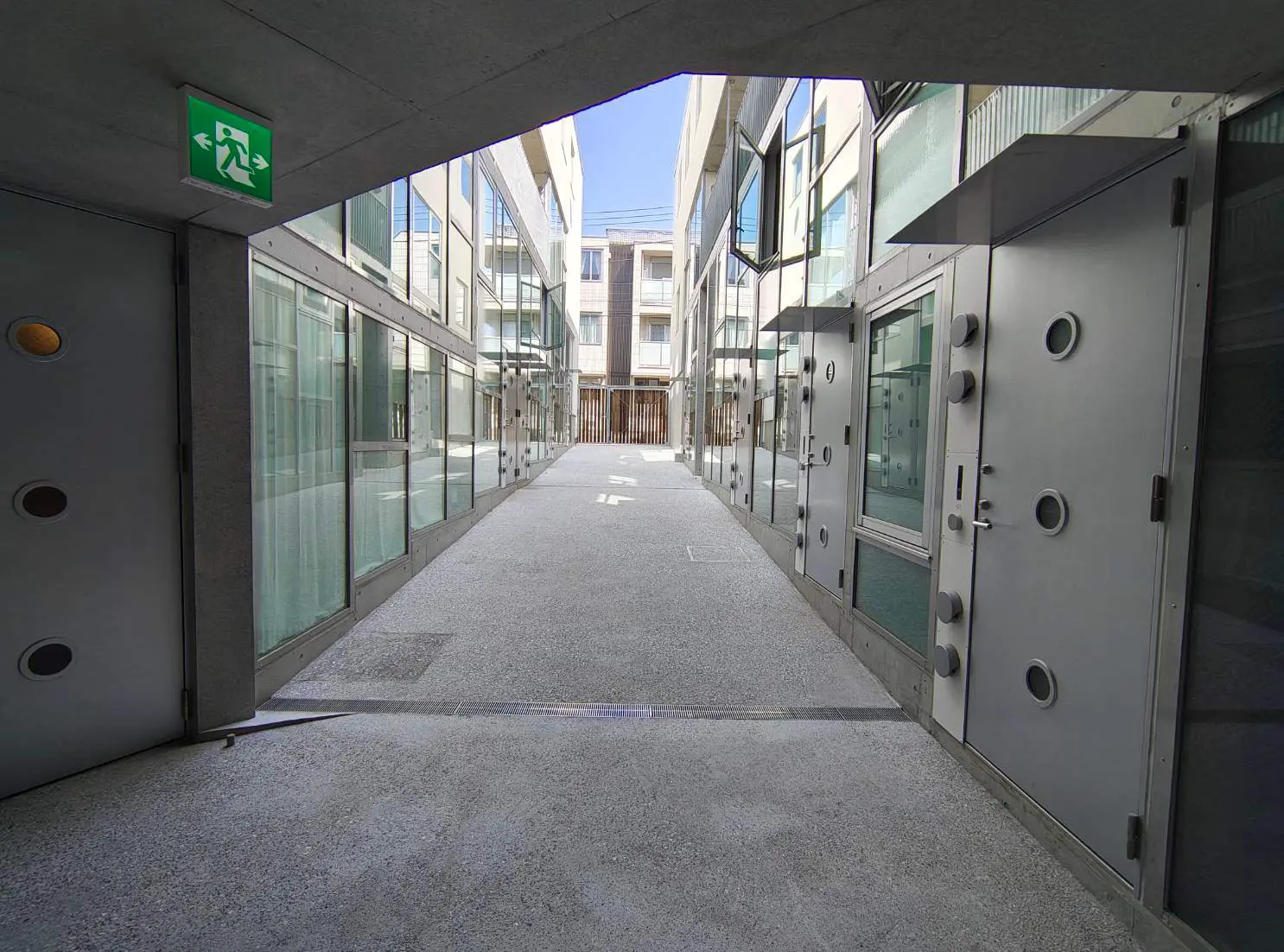 - モダンな建物の中庭、ガラスの壁とメタリックな扉が並ぶ明るい空間、青空が見える風景