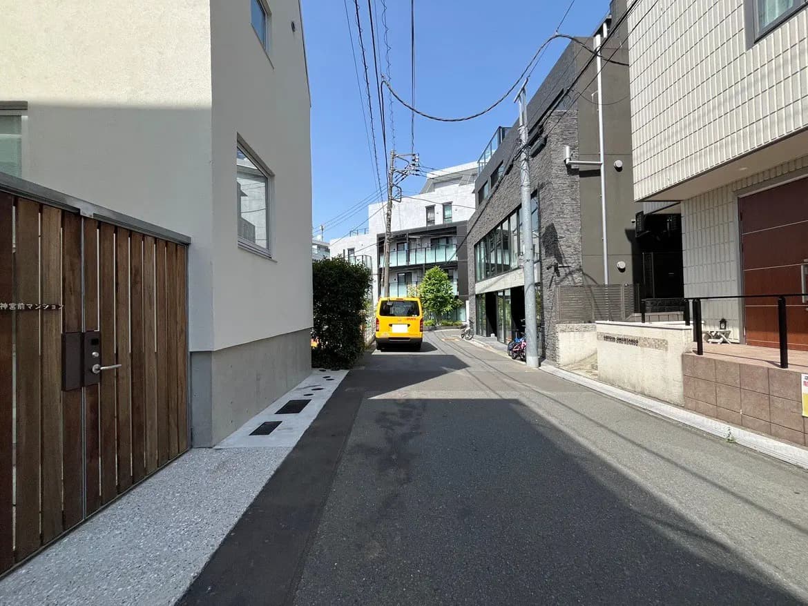 - 都市の住宅街の一角、黄色い車が通る狭い道路と近隣の現代的な建物の風景