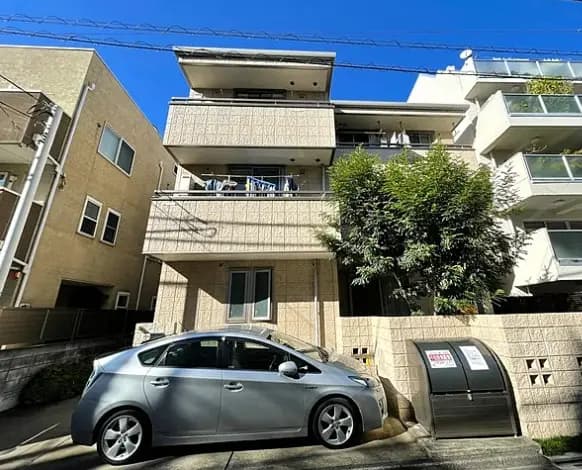 日本の都市部にあるモダンなアパートメントビル、駐車スペースにグレーの車が停まっている外観