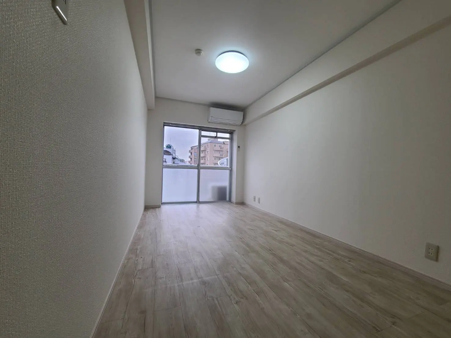 明るく広々とした空の部屋、木目調の床材、白い壁、大きな窓からの自然光