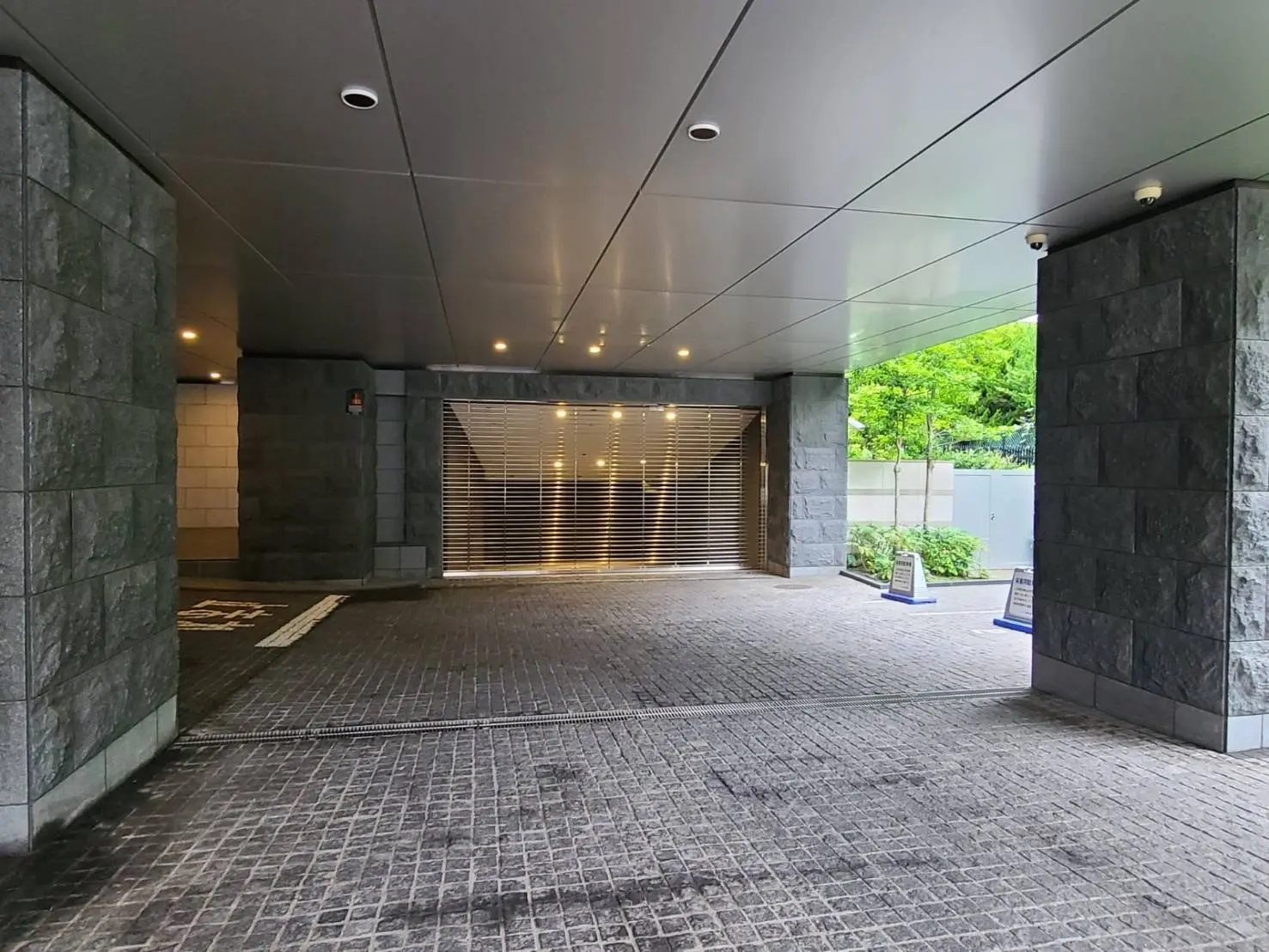 石造りの壁と地面が特徴的なモダンなビルのエントランス、天井には照明が取り付けられ開放的な空間
