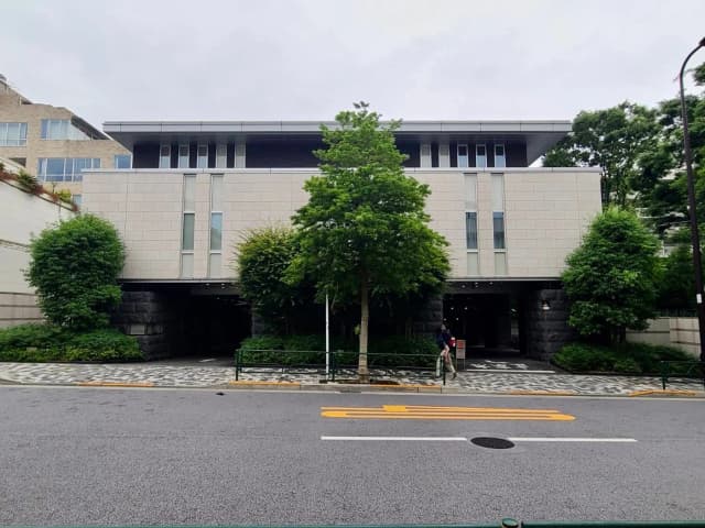現代的なデザインのビルの入り口、緑豊かな樹木と人が歩く歩道