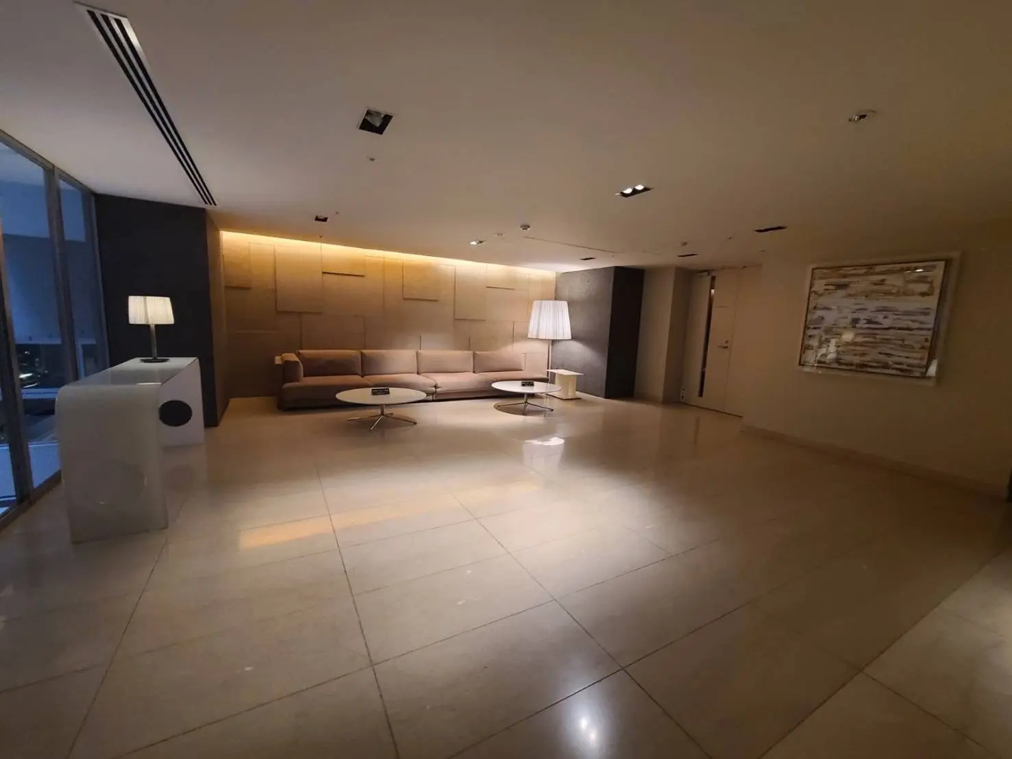 広々としたモダンなロビー、ベージュの壁と床、ソファとコーヒーテーブル、アートフレームと照明付きのインテリア