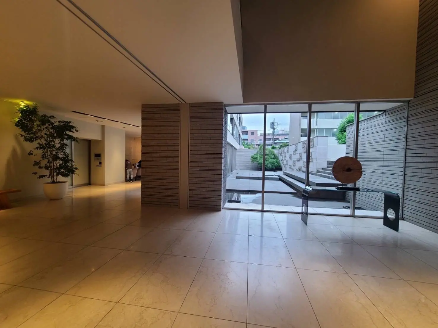高級感のあるホテルのロビー、大理石の床、壁に縦長の照明、大きなガラス窓と屋外の眺望