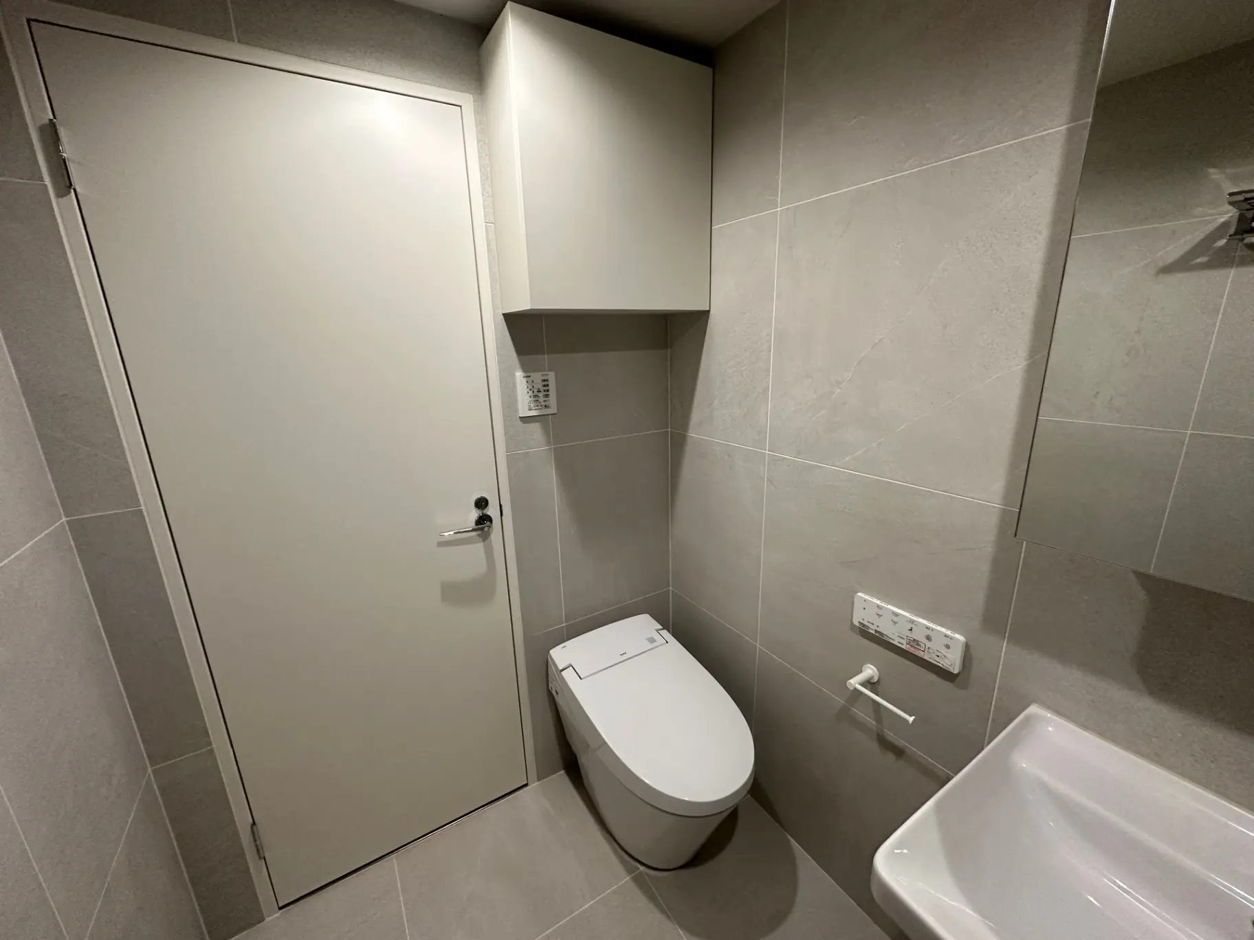 シンプルなグレーのタイルで仕上げられたモダンなバスルーム、白いトイレと浴槽、清潔感のあるインテリア