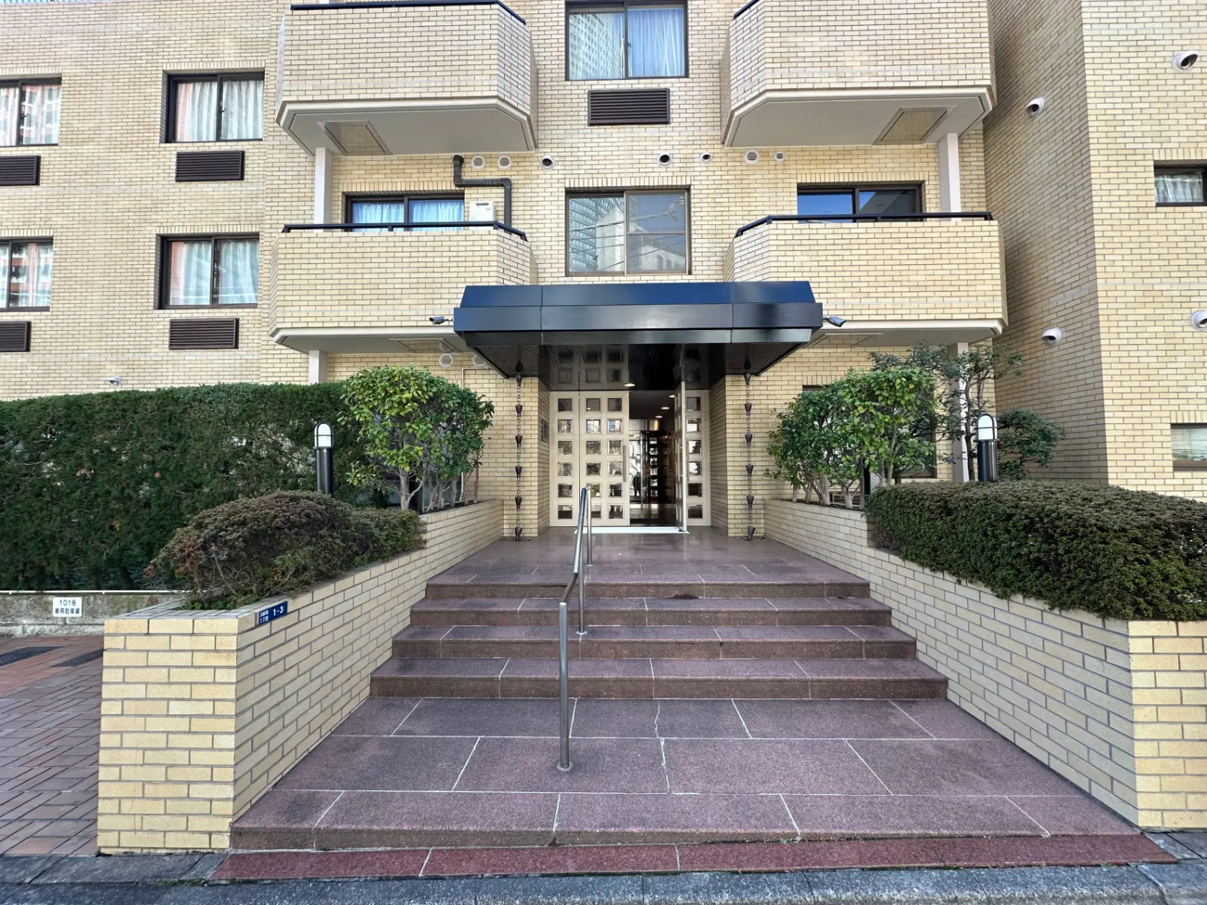 マンションのエントランス、綺麗に整えられた植栽と階段、入り口の上に設置されたアウトドアライト