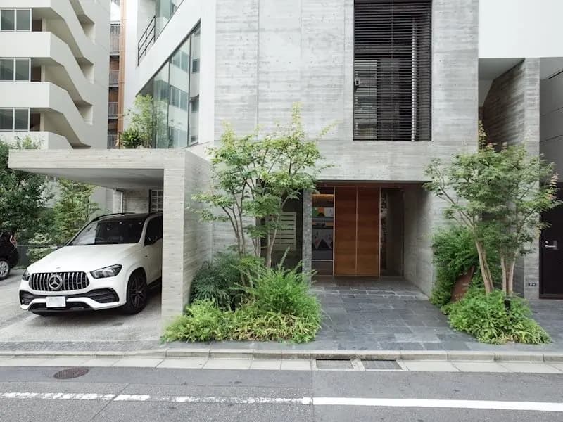 都会的なモダンな外観の建物とカーポート、ホワイトの高級車、緑豊かな植栽