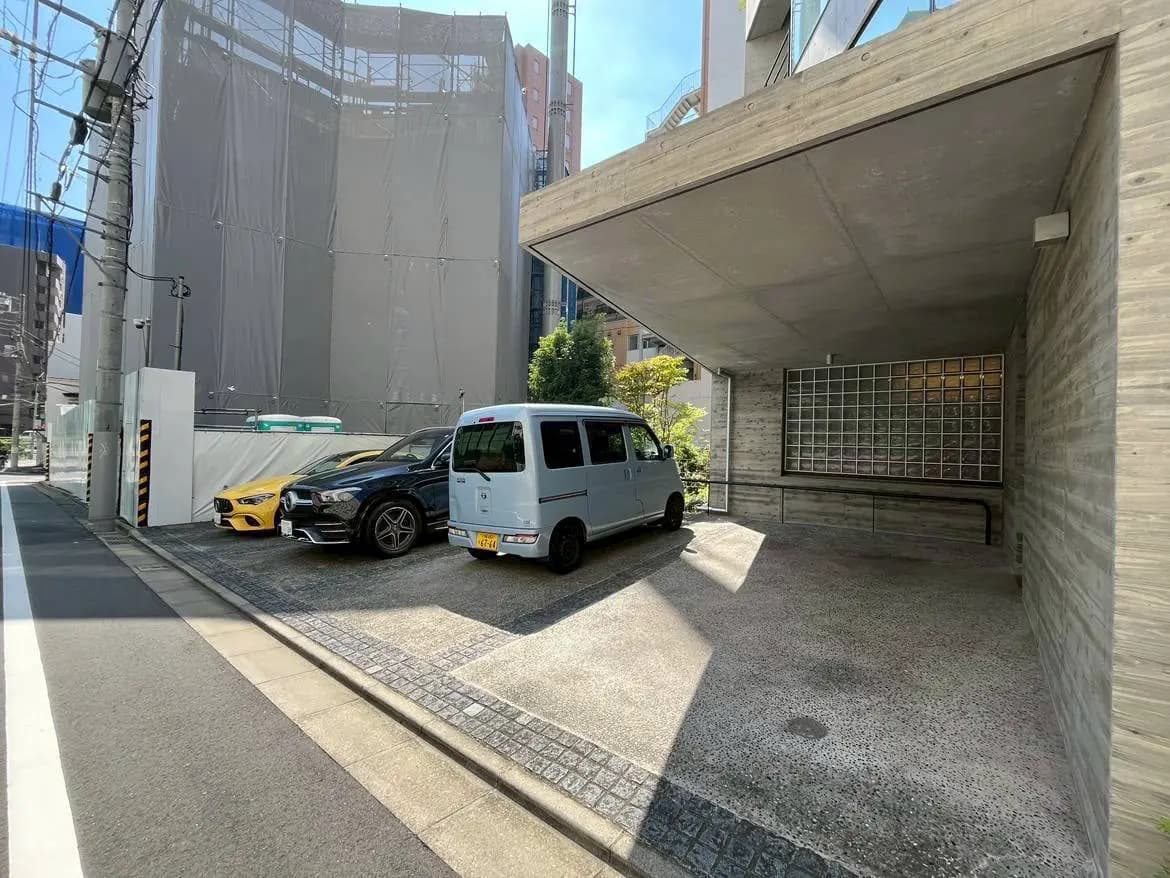- 現代的なデザインの駐車スペースに停まっている2台の車、コンクリートの壁とガラスブロックがある建物の外観と青空の風景