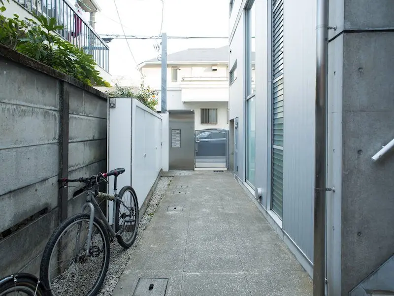 狭い路地と駐輪場、灰色の壁と建物の外観、都市の住宅地