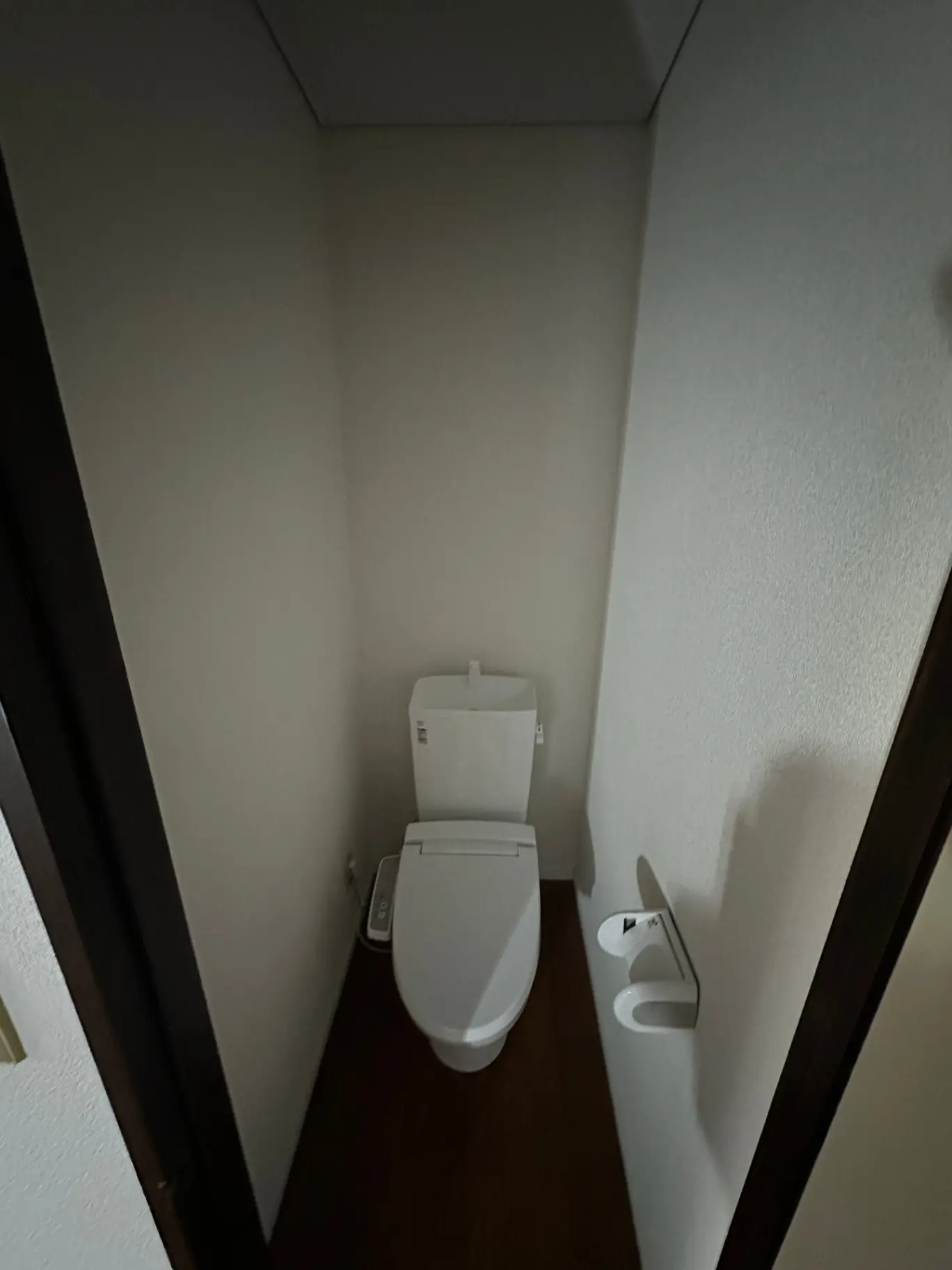 狭いトイレの空間、木目調のフロア、シンプルな白いトイレットペーパーホルダー