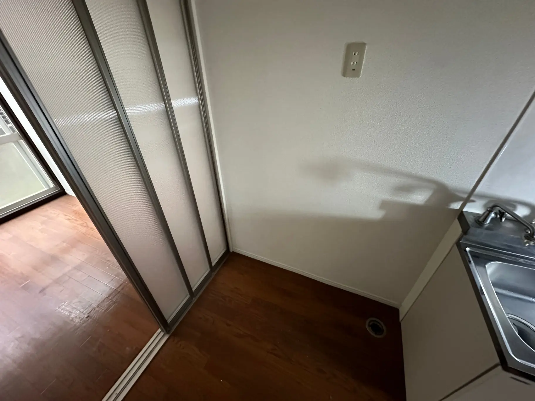 木製フローリングのある空の部屋、スライド式のクローゼット扉と小さなシンクがついたコーナー