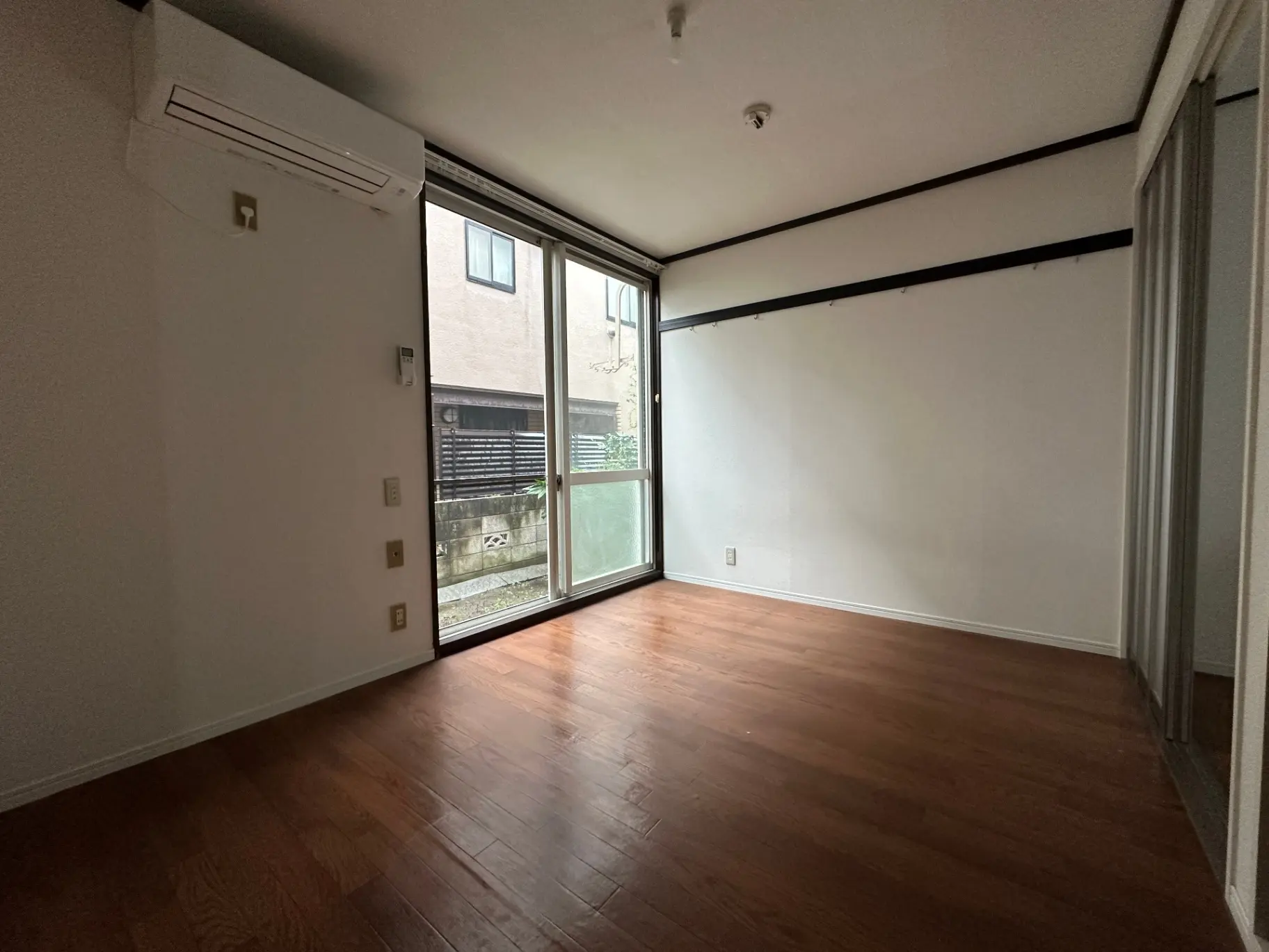 空の部屋、滑らかな木製フローリングと大きな掃き出し窓が付いており明るい自然光が差し込むインテリア