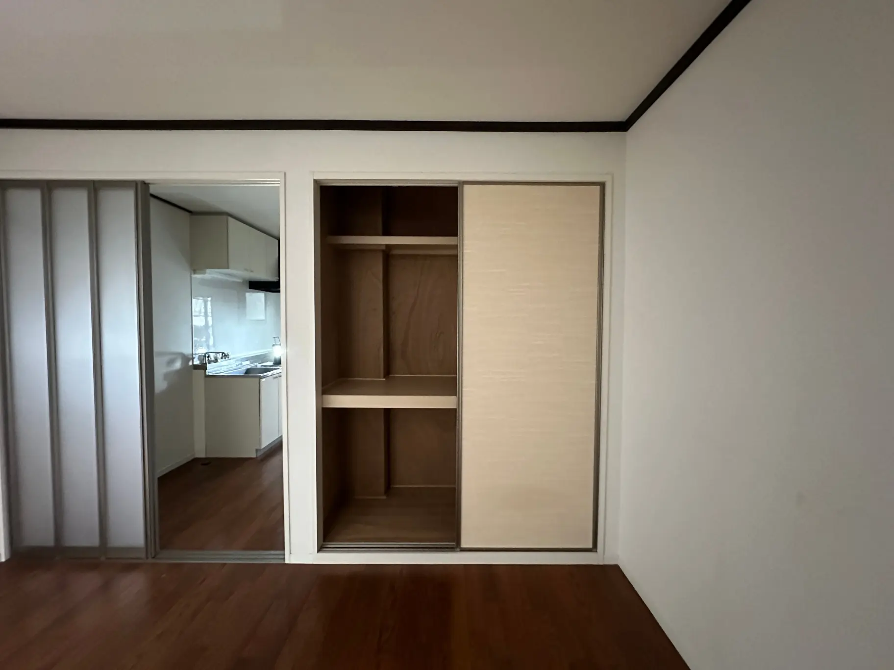 シンプルでモダンなデザインの空の部屋とキッチン、木製フローリングと白い壁、クローゼットの内部ストレージ