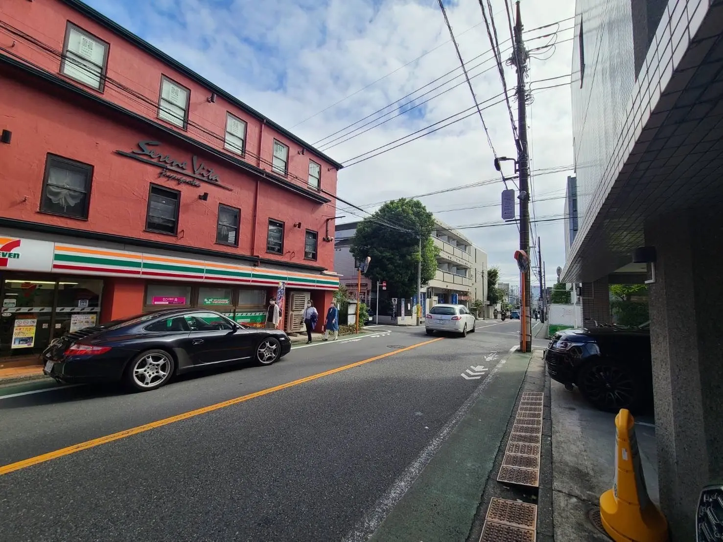 日本の都市の通りの様子、コンビニエンスストアと赤い建物、通行する車と歩行者、晴れた日の街角