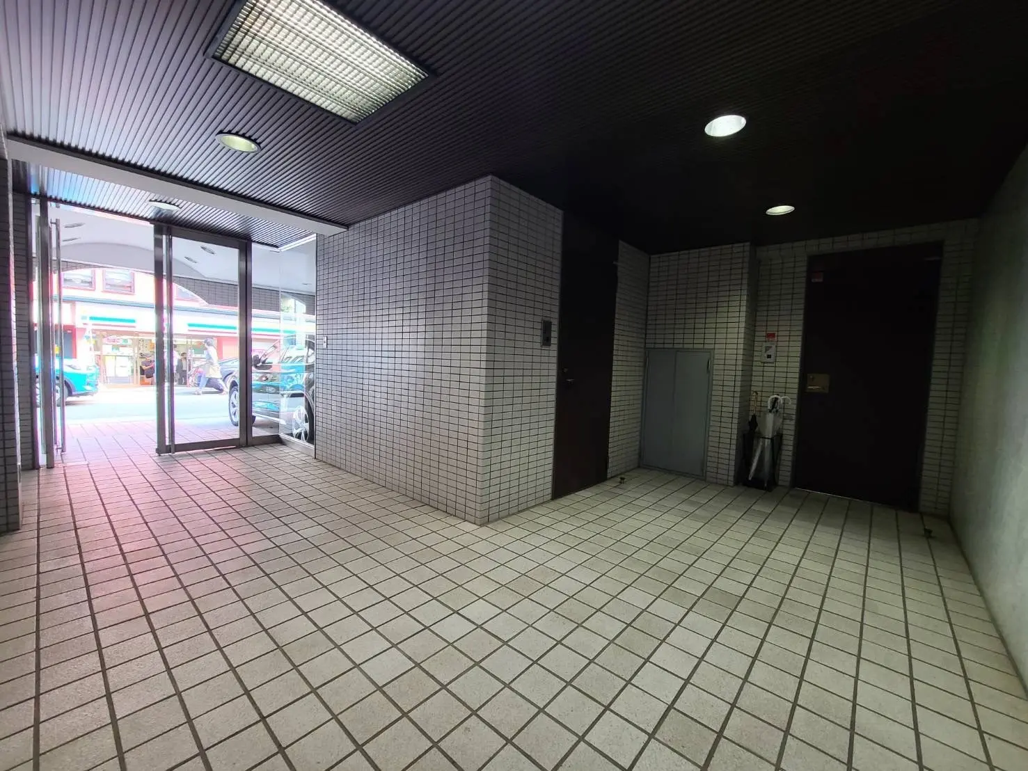建物の入り口の屋根付き通路、白いタイルの床、壁にある扉とゴミ箱