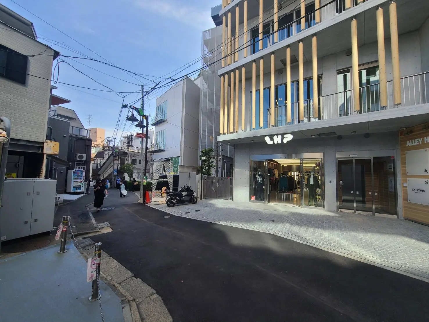 都会のファッション街並み、モダンなビルとおしゃれな服屋、歩行者とバイク、日本の街角