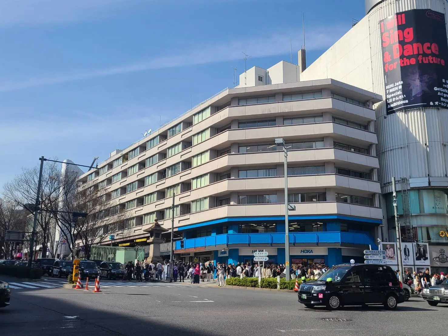 都市の交差点、歩行者が並んで待っている様子、ビルと看板、車が通る光景