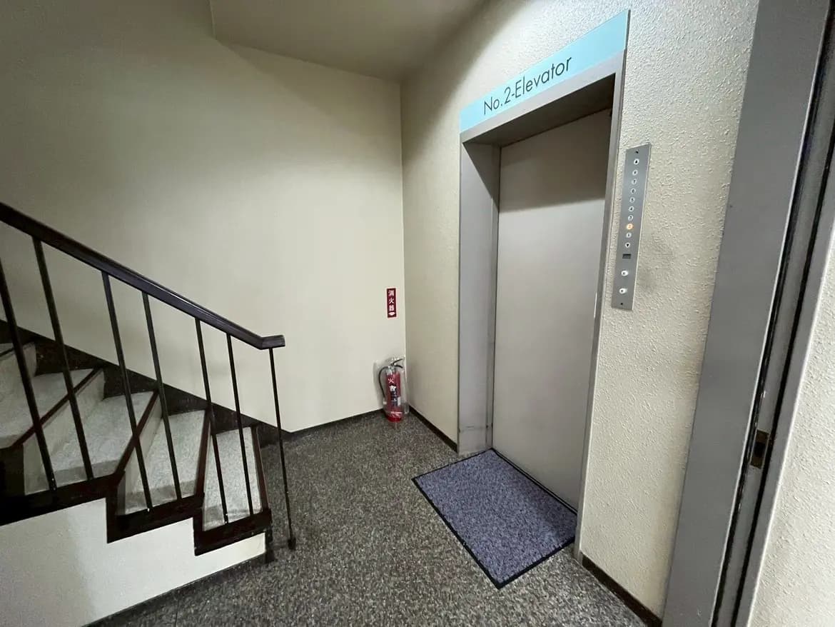 - 鉄製の階段とエレベーターの入口、シンプルな内装と消防用具が見える建物のエントランスエリア