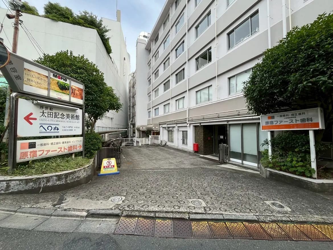 - 太田記念美術館への道標があるエントランス、周囲には緑豊かな植栽と近代的な建物の外観が見える風景