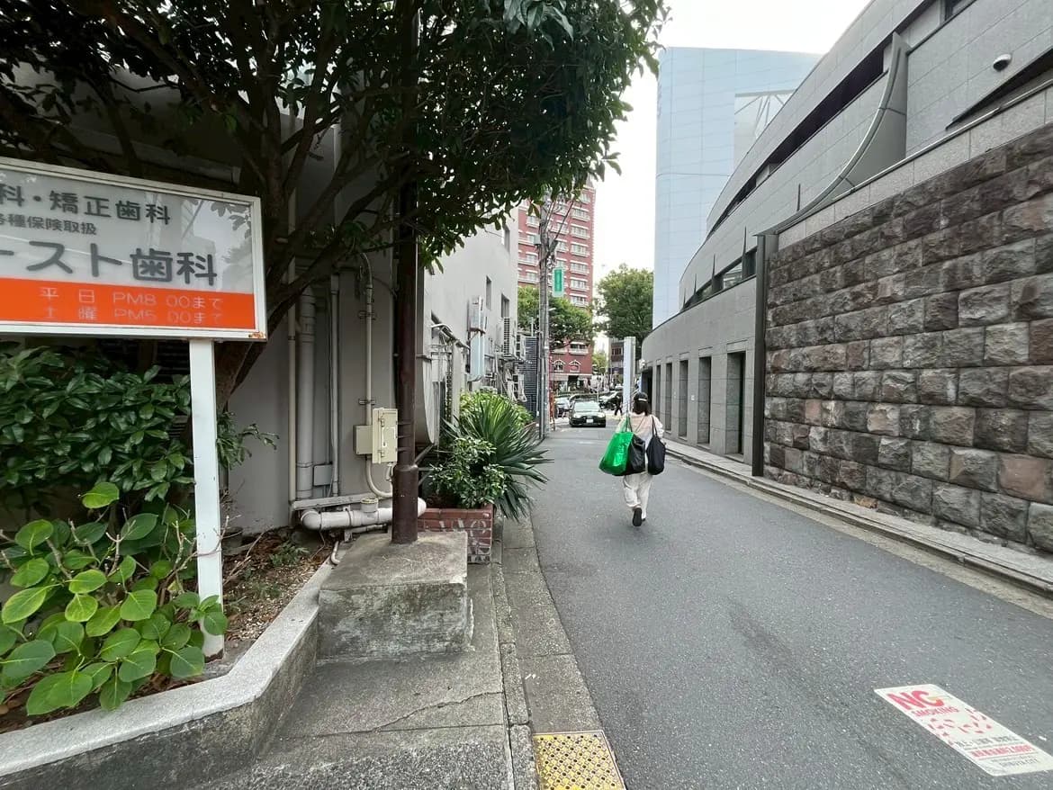 - 医療看板のある狭い路地を歩く女性、周囲には緑があり近代的な建物が立ち並ぶ風景