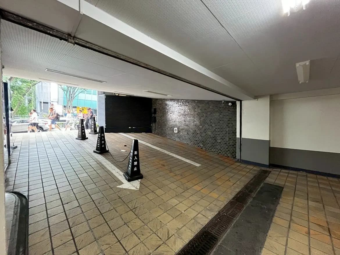 - 駐車場の入口付近、進入禁止の看板が立つタイル敷きの通路と背後の壁が映る画像