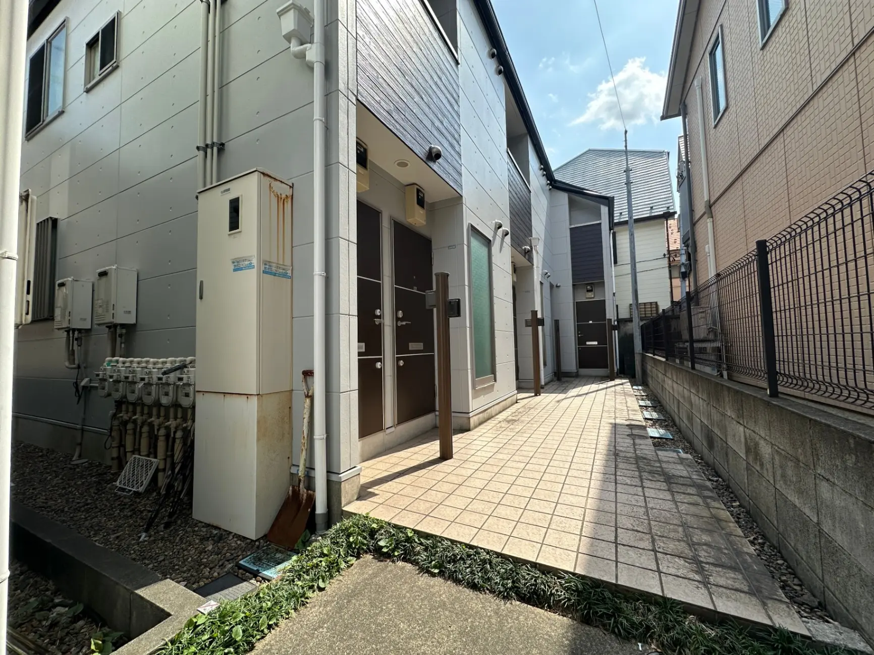 都市型アパートメントの外観、タイル張りの通路、銀色の外壁とガスメーターが設置されたエントランス