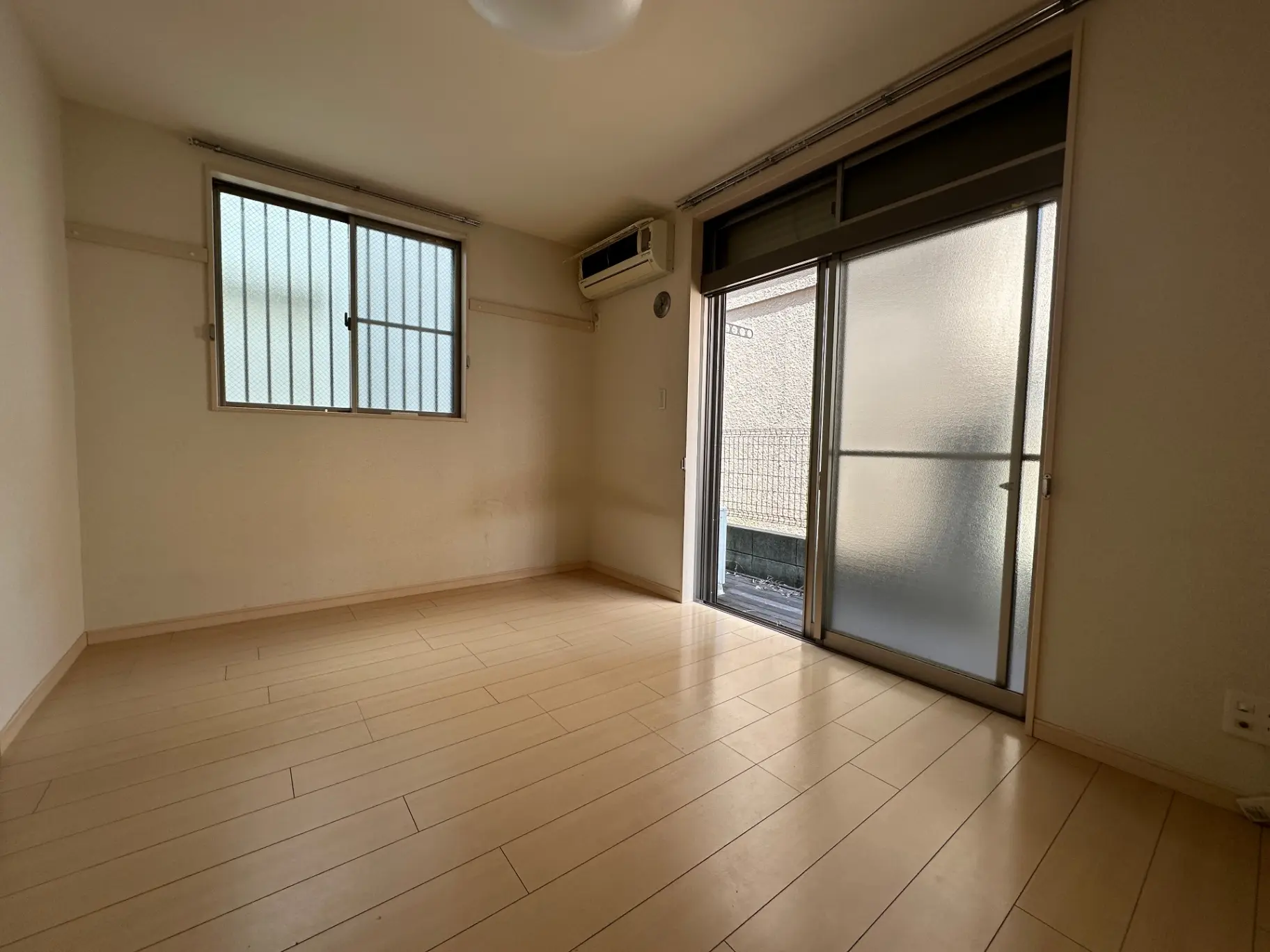 広くて明るいリビングルーム、白い壁とベージュのフローリング、大きな掃出し窓からの自然光