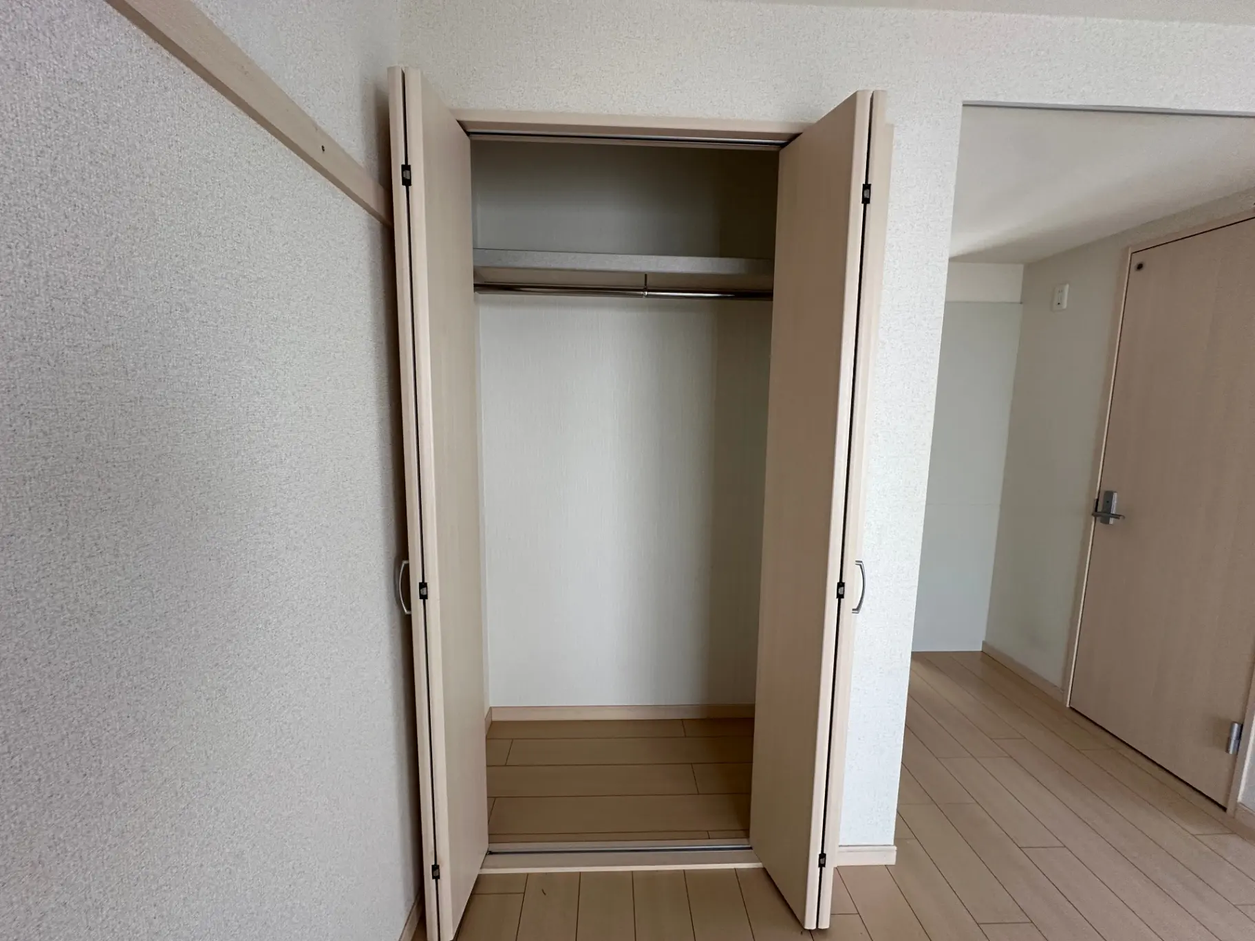 新築マンションの空のクローゼット、木製の引き戸と棚、床はライトブラウンのフローリング