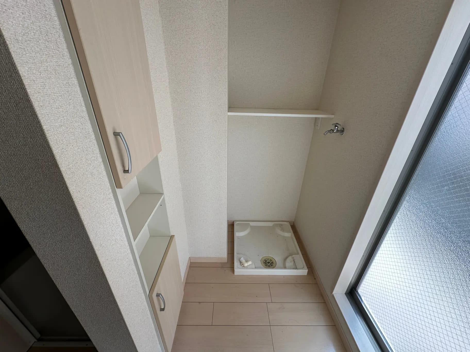 コンパクトな洗面所、白い壁と木目調の棚、フロストガラスの窓がついたインテリア