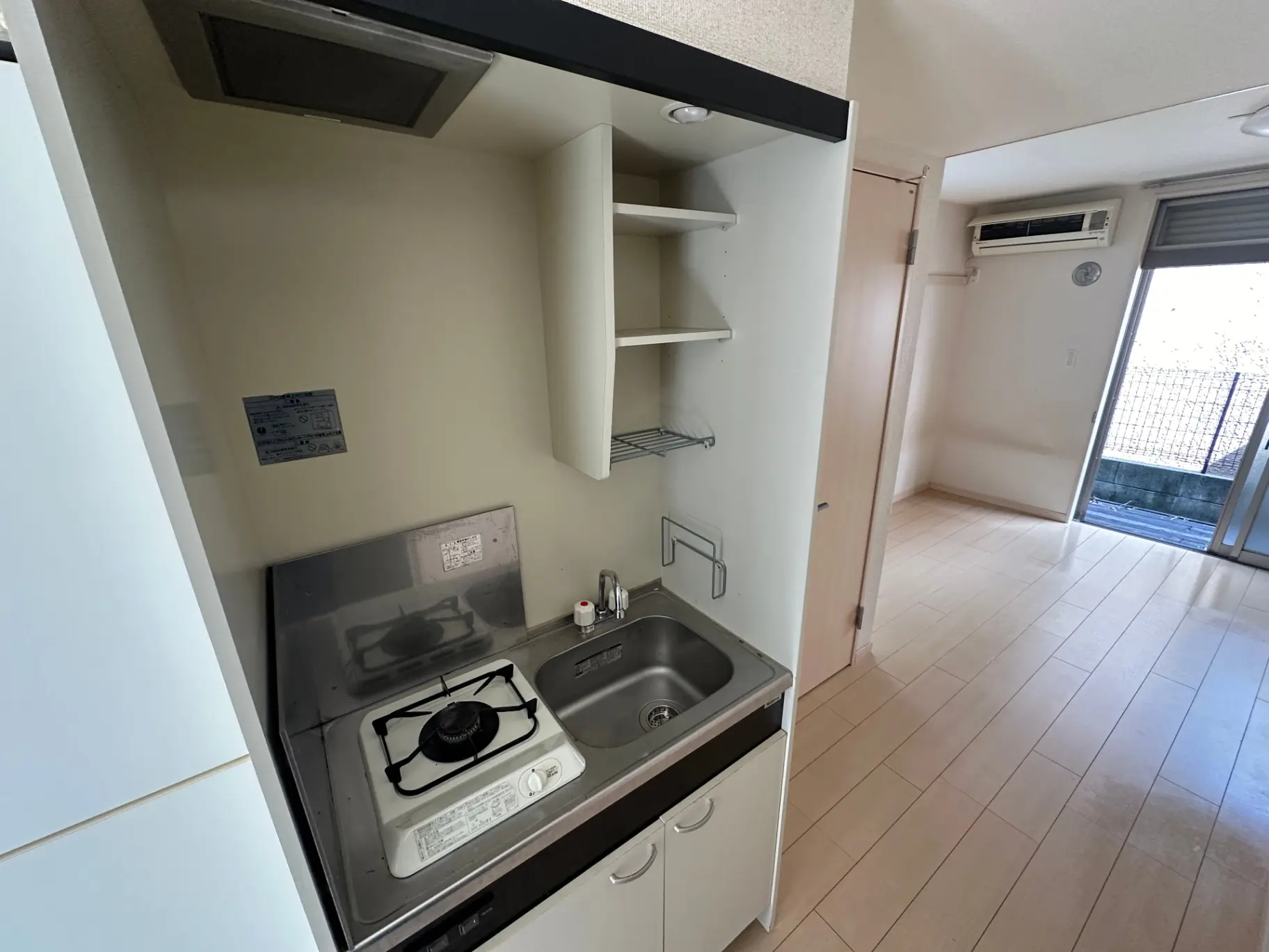 コンパクトなキッチンスペースとバルコニー付きのワンルームアパートメント、ガスコンロとシンクが備え付けられた清潔感のある内装