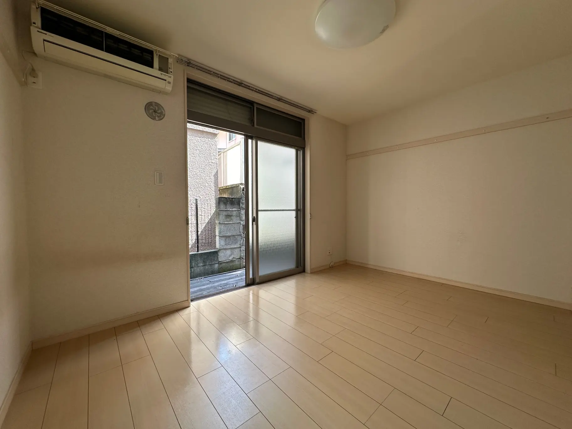 明るく広々としたリビングルーム、エアコン付き、バルコニーへの滑り出し窓、木目調のフローリング